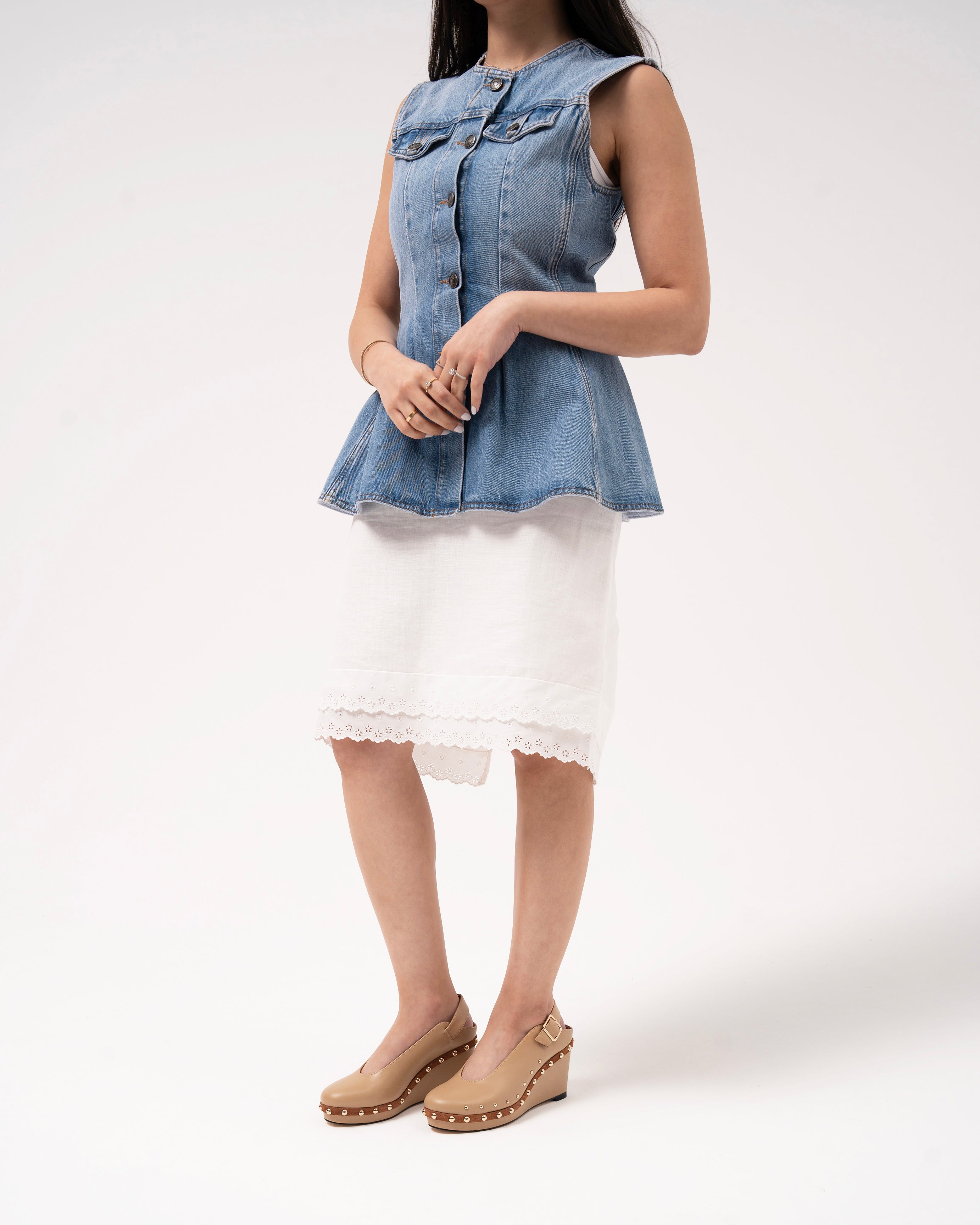 Woman in denim peplum top, white lace skirt, and beige studded wedge heels for everyday style